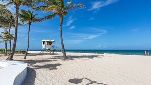 Una playa con una torre de salvavidas, palmeras y un cielo azul despejado.