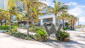 Un hotel moderno con un gran letrero en forma de 'W', palmeras y un camino pavimentado.