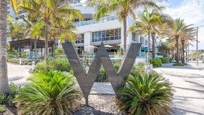 A large 'W' sign in a landscaped area with palm trees and a modern building in the background.