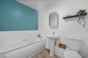 Un baño moderno con una bañera blanca, un lavabo pedestal y un inodoro.