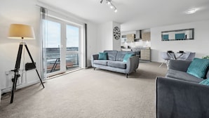 A modern living room with a grey sofa, a lamp, and a view of the sea through large windows. - The Pinnacle by Cotels (Northampton)