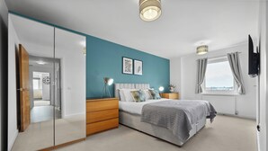 A bedroom with a bed, bedside tables, a wardrobe, a window with curtains, and a TV mounted on the wall. - The Pinnacle by Cotels (Northampton)