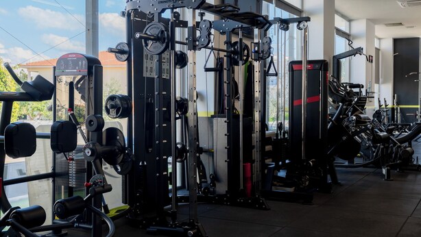 Un gimnasio con diferentes máquinas de ejercicio, ventanas amplias y vistas al exterior.
