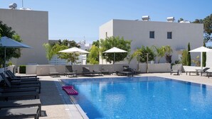 Una piscina con sillones y sombrillas, rodeada de edificios con depósitos de agua en el techo.