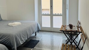 A bedroom with a bed, a small table with a vase, and a door with blinds. - Affittacamere The Shuttle (Livorno)