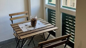 A small balcony with a wooden table and two chairs, a glass vase with dried flowers, and a view of a building through the window. - Affittacamere The Shuttle (Livorno)