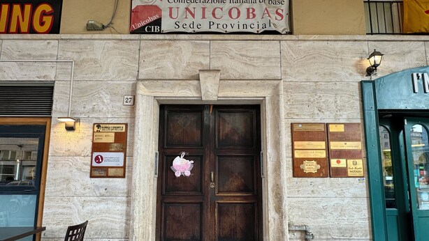A building facade with a large wooden door, a sign for 'Confederazione Italiana di base UNICOBAS Sede Provinciale', and several plaques on the wall. - Affittacamere The Shuttle (Livorno)