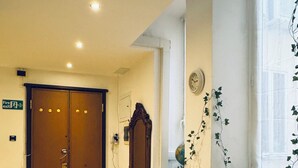 A hotel lobby with a wooden bench, a fire exit sign, a clock, and a window with a plant. - Affittacamere The Shuttle (Livorno)