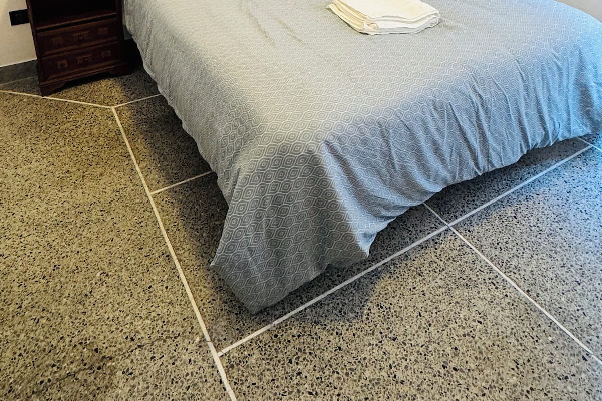 Un lit simple avec une couvre-lit et des oreillers à motifs gris, une table de chevet en bois avec des tiroirs, et une serviette blanche sur le lit.