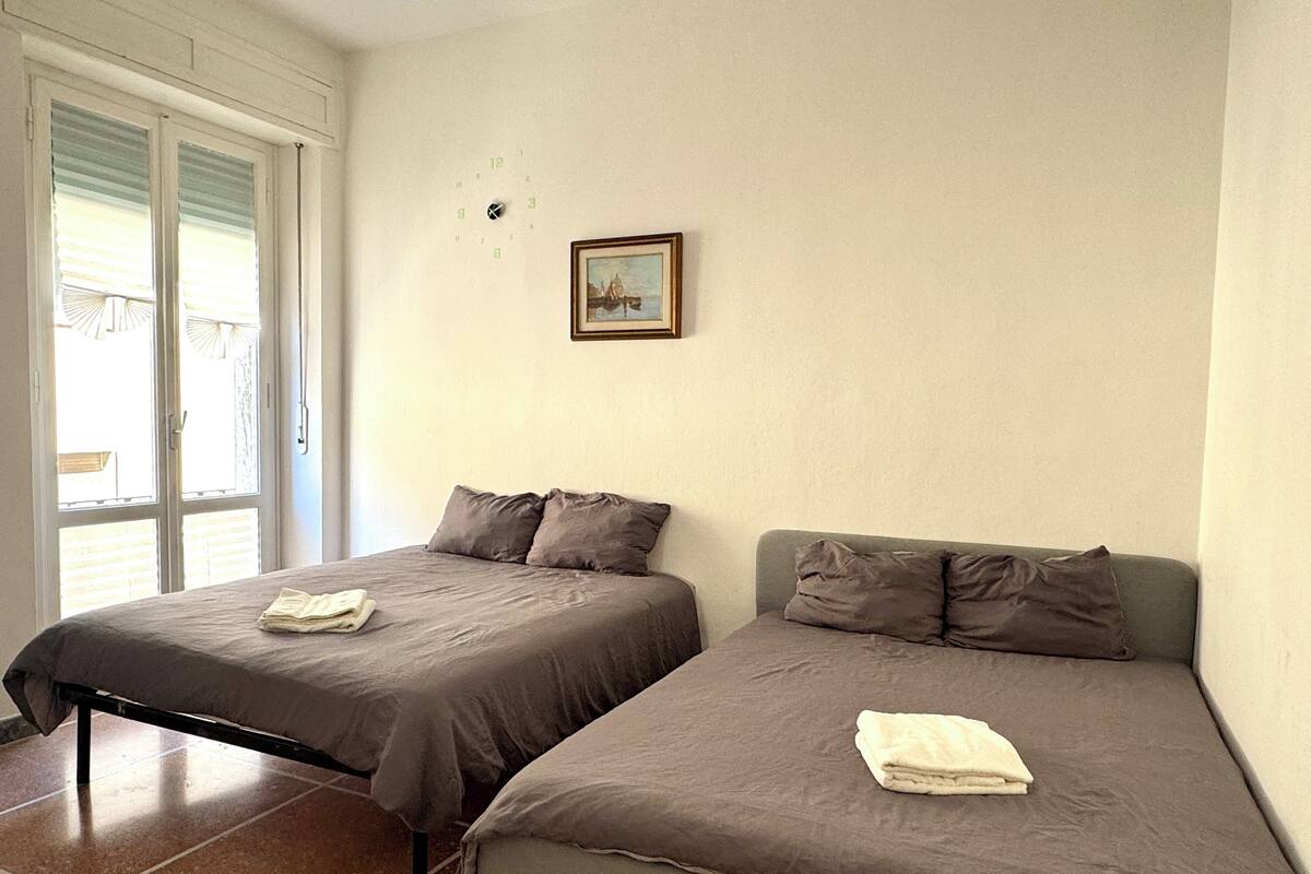Deux lits simples avec une literie et des oreillers gris, un petit tableau encadré accroché au mur et une fenêtre avec des stores.