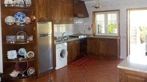 Une cuisine avec des meubles en bois, un réfrigérateur en acier inoxydable, un lave-linge et une fenêtre donnant sur un paysage verdoyant.
