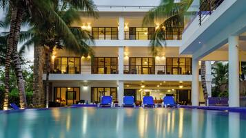 A multi-story hotel with a swimming pool, palm trees, and outdoor seating.