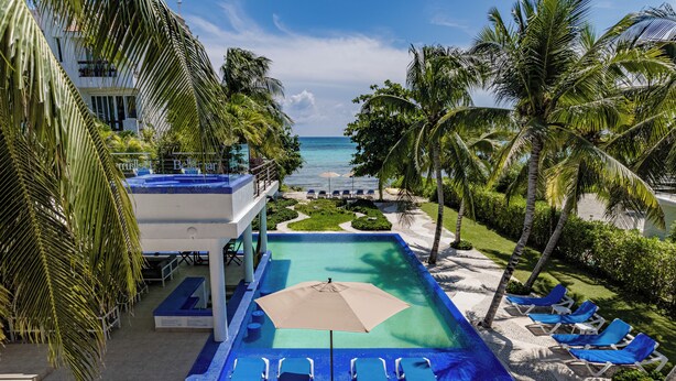 A pool area with lounge chairs and an umbrella, surrounded by palm trees and a view of the ocean. - VILLA BELLAMAR AKUMAL (Akumal)