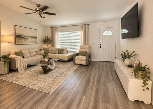 A living room with a sofa, armchairs, a coffee table, and a flat-screen TV mounted on the wall.