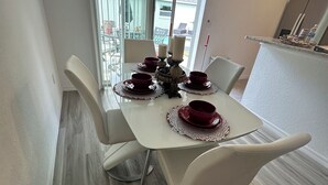 A dining area with a white table set for four, surrounded by white chairs.