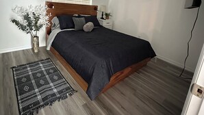 A bedroom with a bed, a ceiling fan, a window with blinds, a nightstand, and a decorative plant.