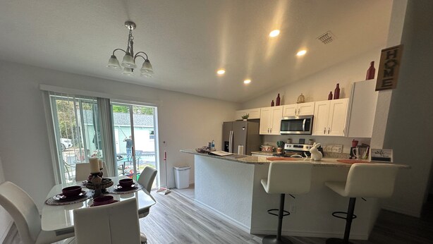 A modern kitchen with white cabinetry, a central island with bar stools, and a dining area with a table and chairs.