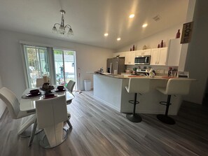 A modern kitchen with white cabinetry, a central island with bar stools, and a dining area with a table and chairs.