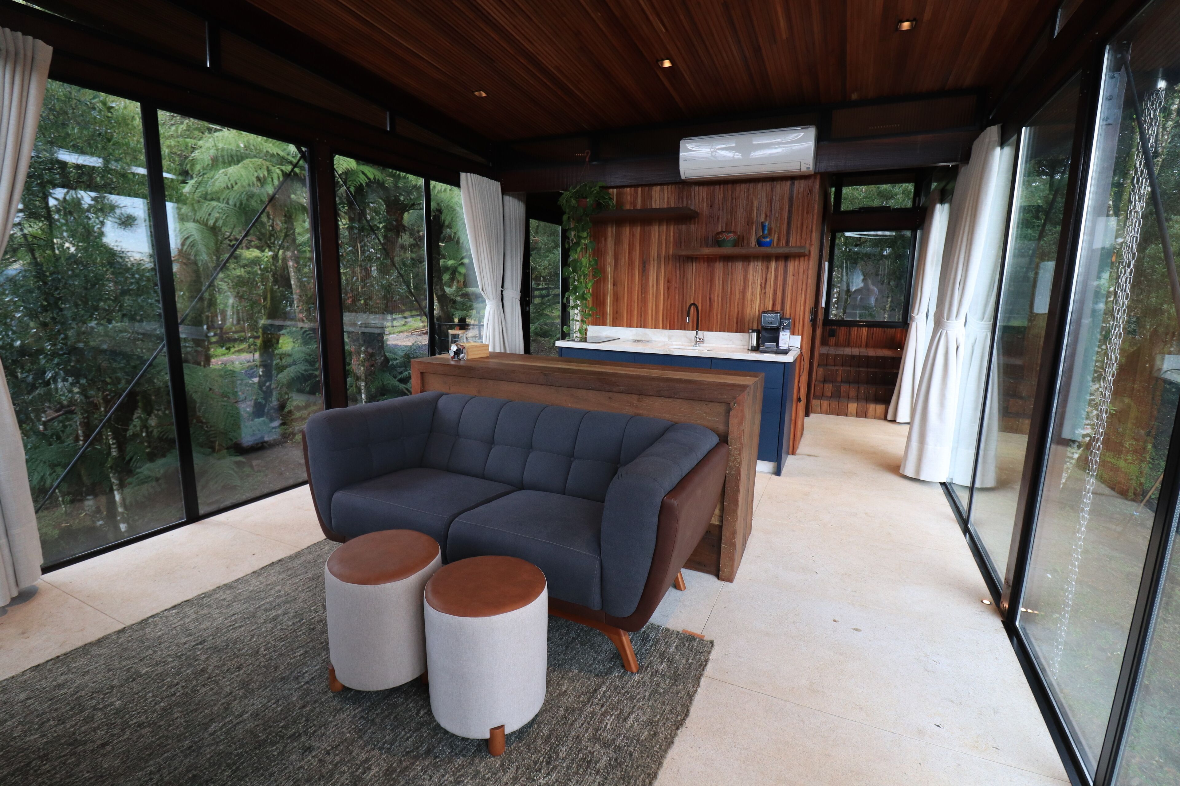 A modern living room with a sectional sofa, two ottomans, and a kitchen area with a sink and counter.