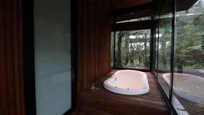 Une salle de bain moderne avec un plancher en bois, une grande baignoire et une vue sur une forêt, visible à travers de grandes fenêtres.