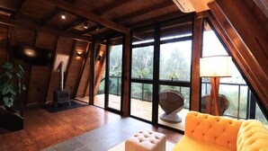 Une pièce spacieuse avec un plafond en bois, de grandes fenêtres, un canapé jaune et une petite table avec une lampe.
