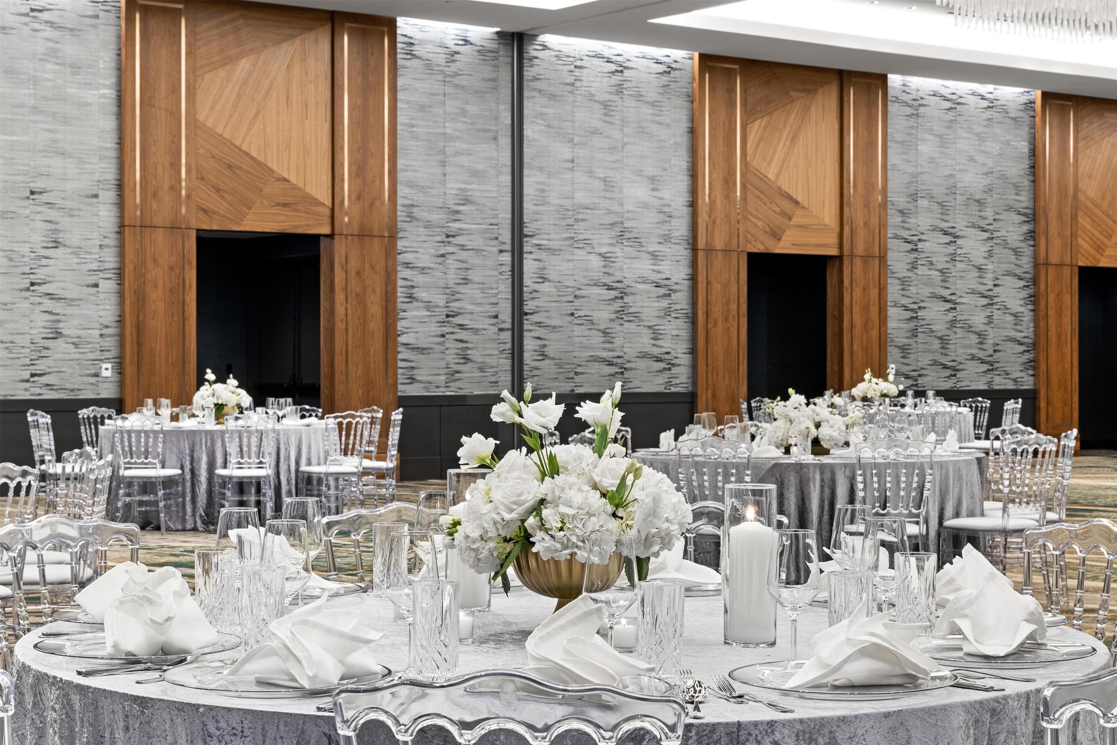A banquet hall with round tables set for a formal event, featuring white tablecloths, crystal glassware, and floral centerpieces.