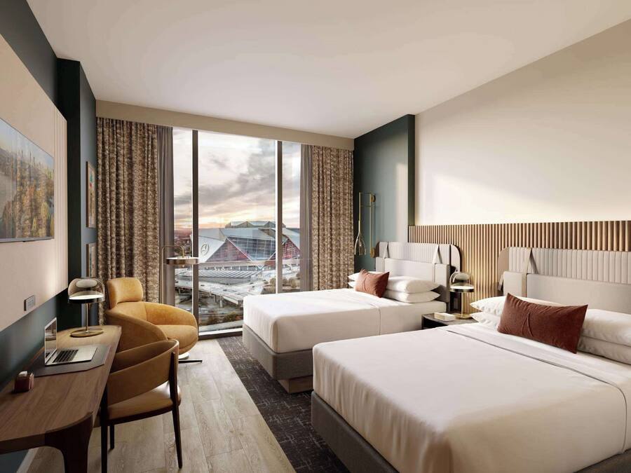 Quarto de hotel com duas camas, uma escrivaninha, uma cadeira e uma janela grande com vista para a cidade.