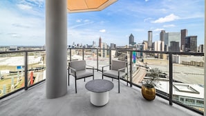 Un balcon avec vue sur la ville, deux chaises, une table et un pot de fleurs.