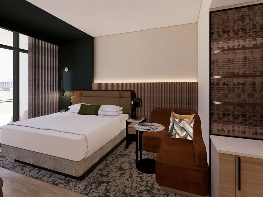 A modern hotel room with a large bed, a small sofa, a desk, and a view of the cityscape.