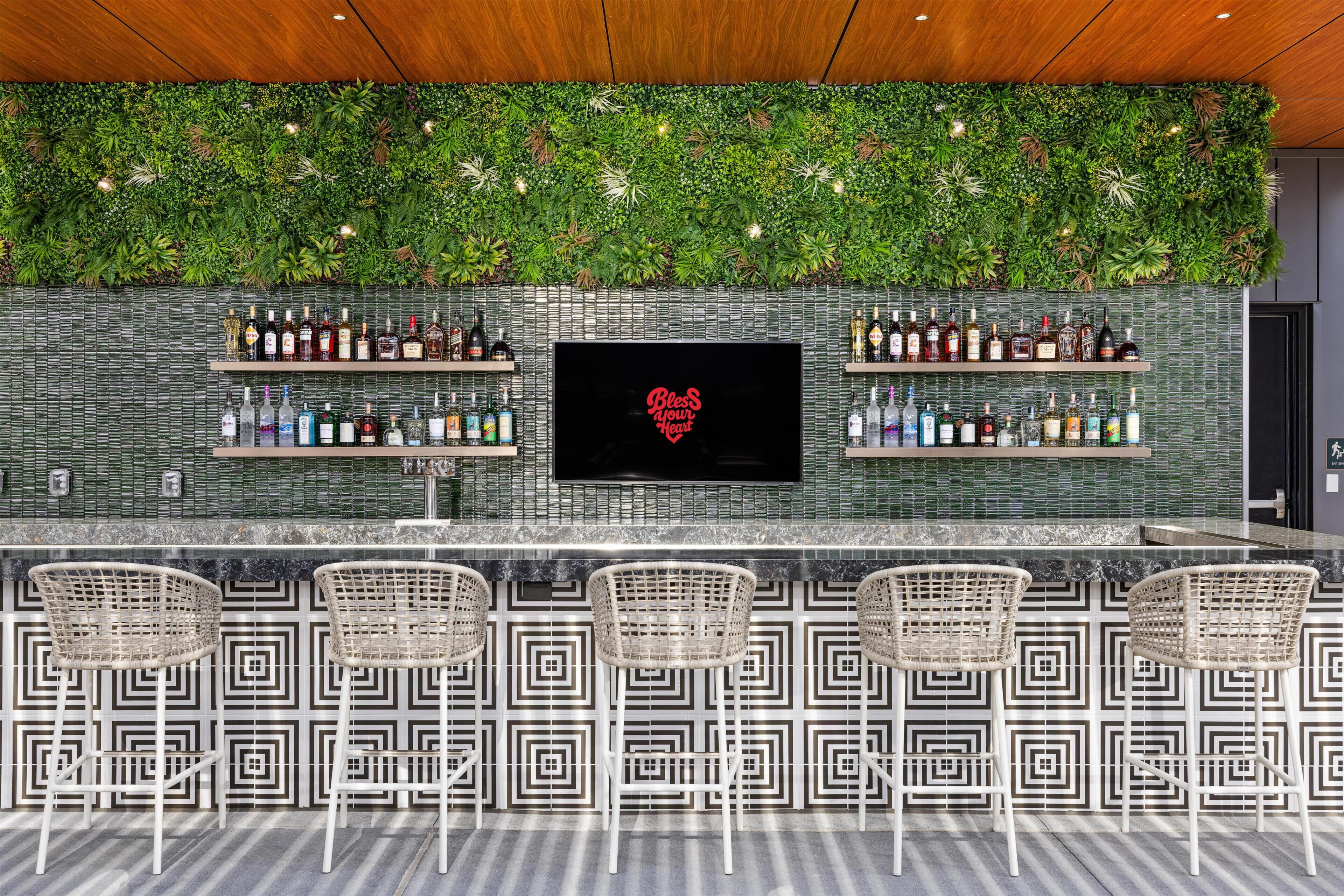 A bar area with a green leafy wall, a flat-screen TV, and multiple liquor bottles.