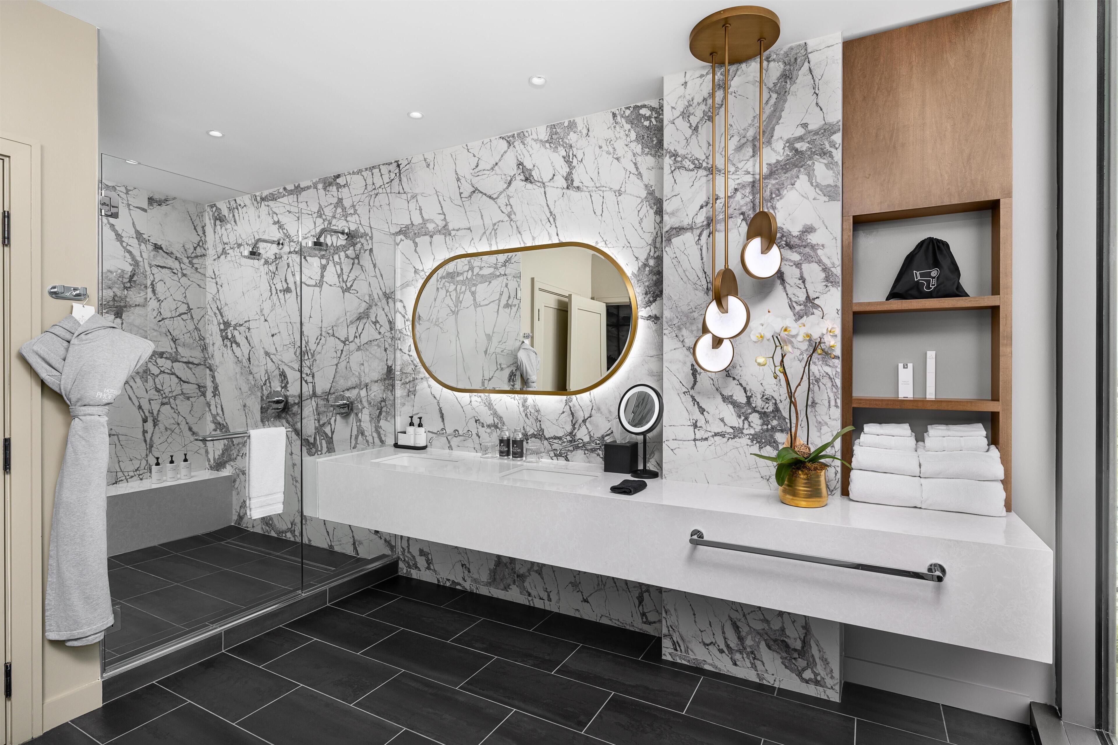 Un baño moderno con pared de mármol, un espejo grande, tocador con perchero y zona de ducha.