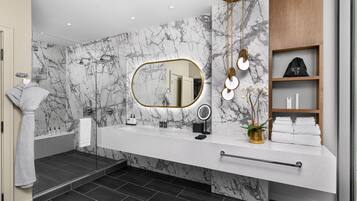 Un baño moderno con pared de mármol, un espejo grande, tocador con perchero y zona de ducha.