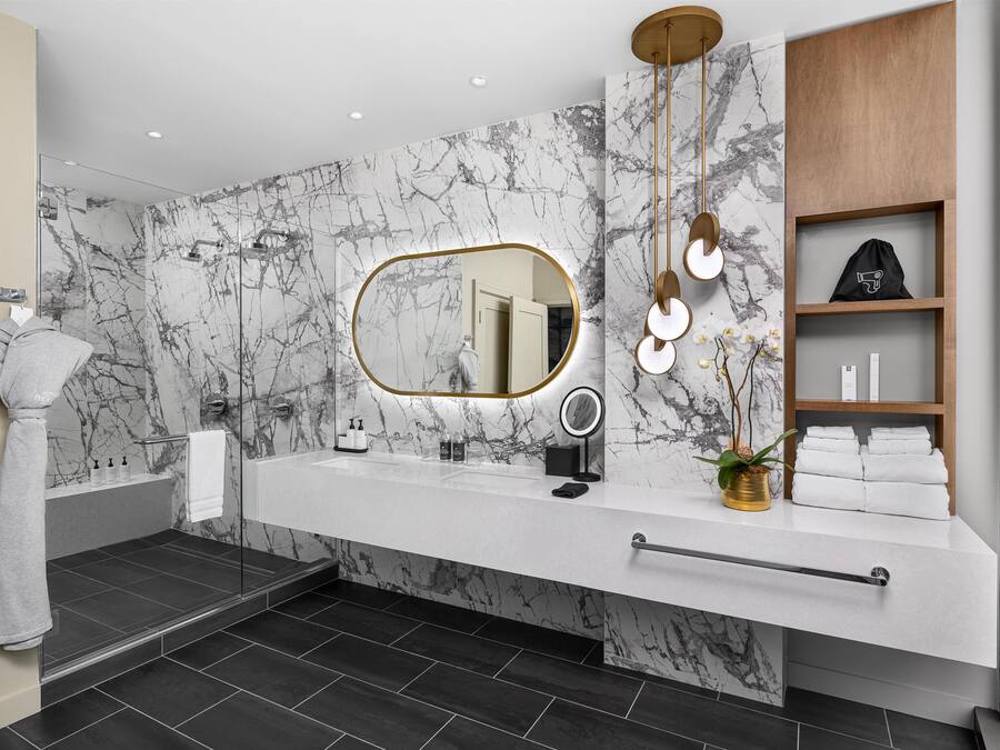 Un baño moderno con pared de mármol, un espejo grande, tocador con perchero y zona de ducha.