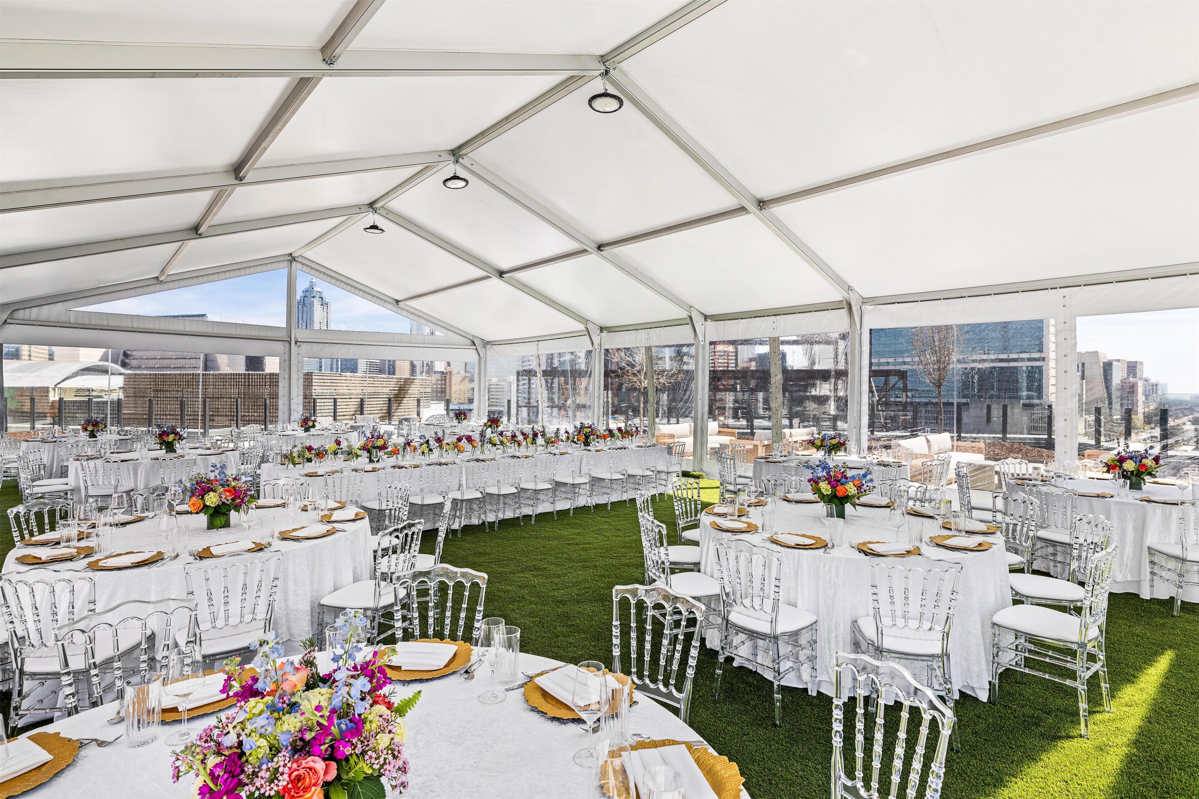 A tented event space with round tables, white chairs, and floral centerpieces.