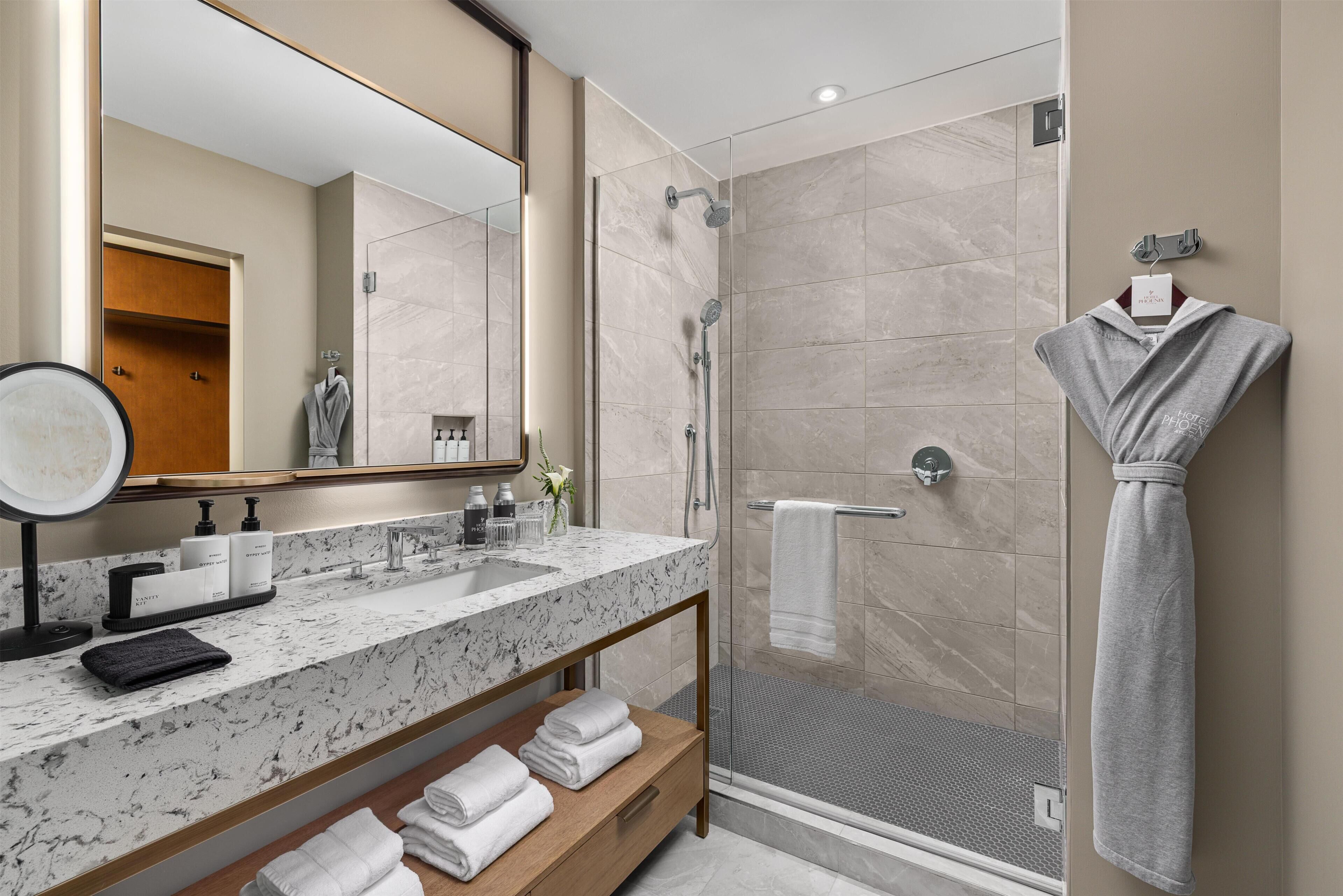 A modern bathroom with a marble sink, a glass shower enclosure, and a robe hanging on the wall.