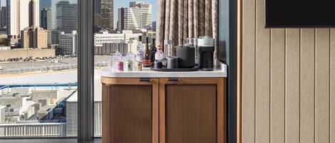 Vista de la ciudad desde una ventana, una kitchenette con cafetera y un televisor montado en la pared.