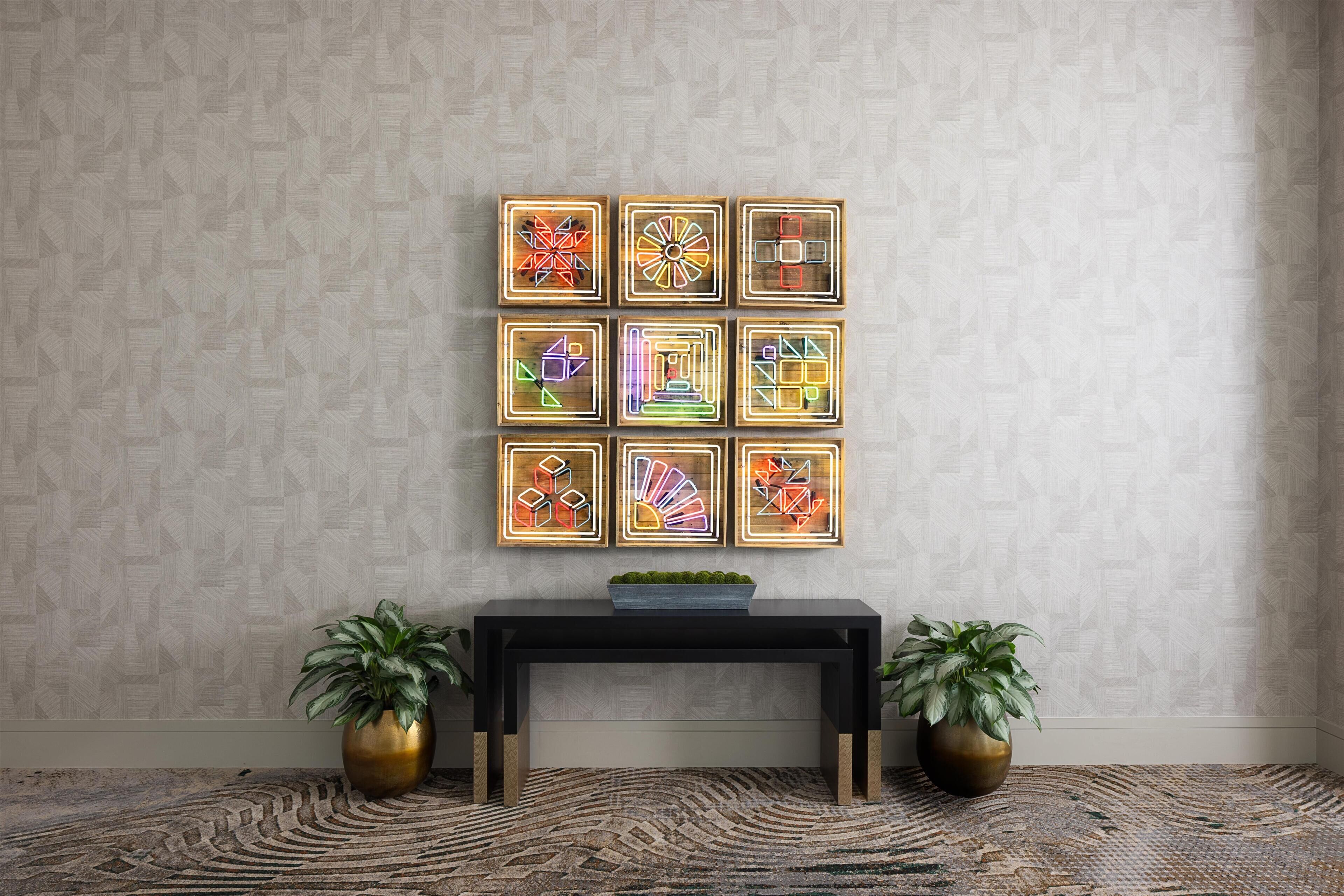 A room with a patterned wallpaper, a black console table with a plant, and framed abstract art on the wall.
