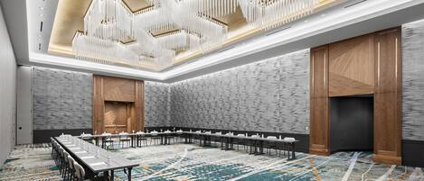 A conference room with a long table, white chairs, and a patterned carpet.