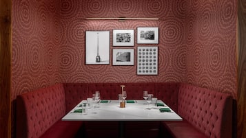 A red upholstered booth with a white table set for dining, featuring framed pictures and a wall clock.