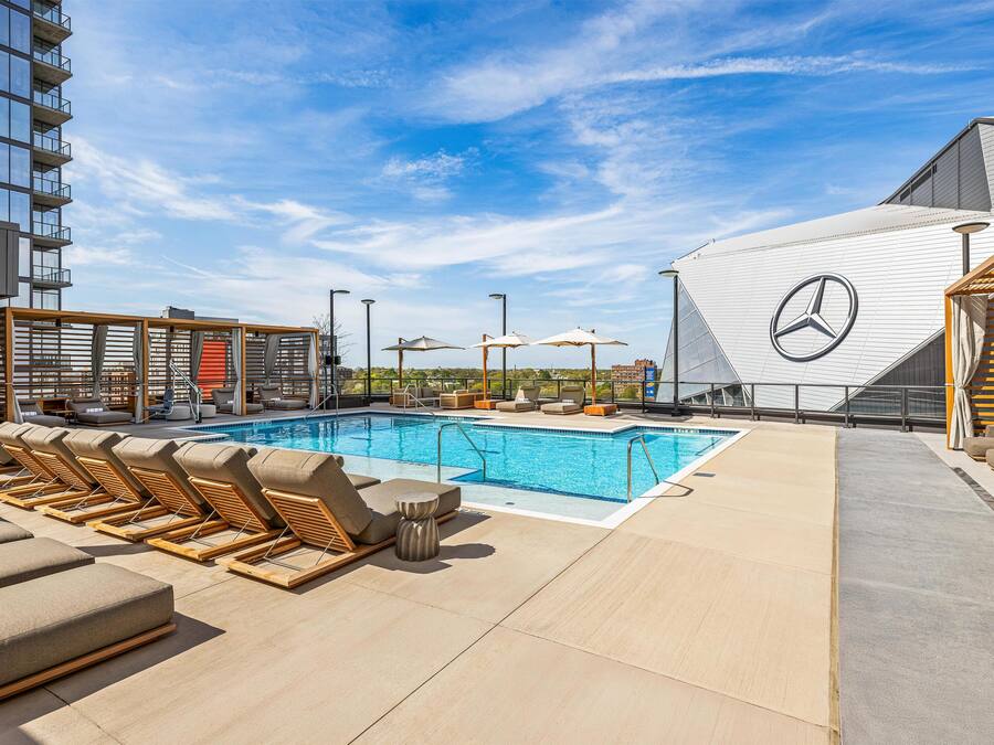 A rooftop pool area with lounge chairs and umbrellas, a Mercedes logo, and a modern building in the background.