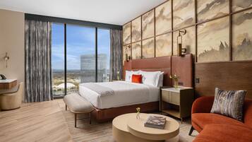 Une chambre d’hôtel moderne, dotée d’un grand lit, d’un canapé, d’une table basse ronde et offrant une vue sur le paysage urbain.