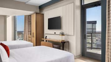 A hotel room with two beds, a desk, a TV, and a large window with a city view.