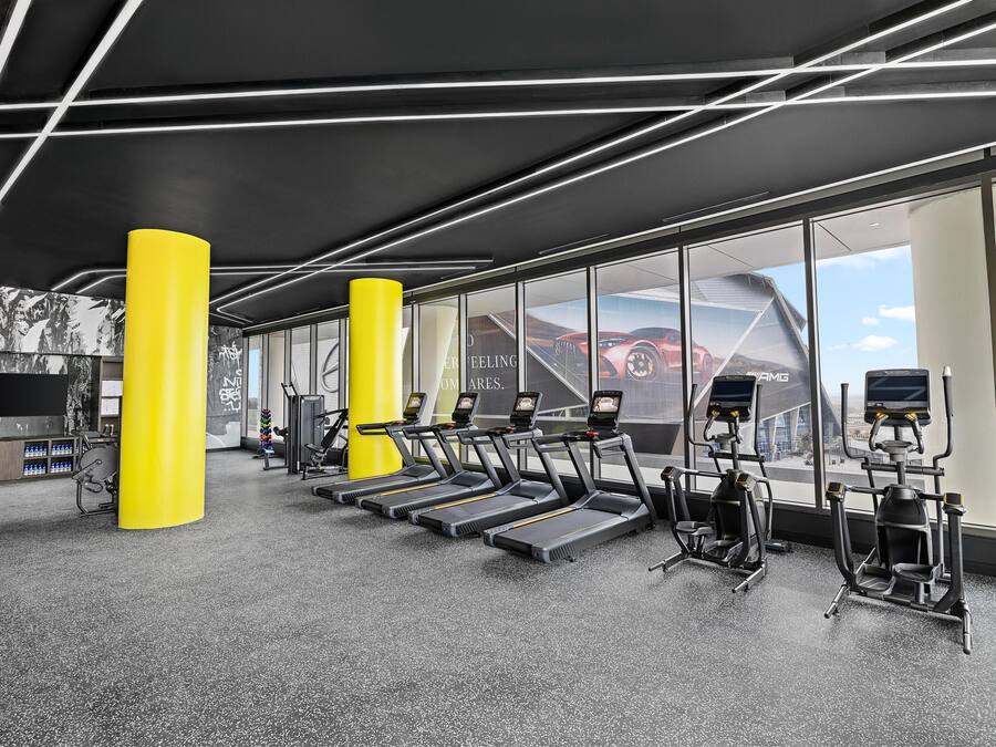 A gym with treadmills, elliptical machines, and a large window with a view of a red car and a building.