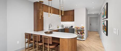 A modern kitchen with a central island, bar stools, pendant lighting, and a view into the adjacent living area.