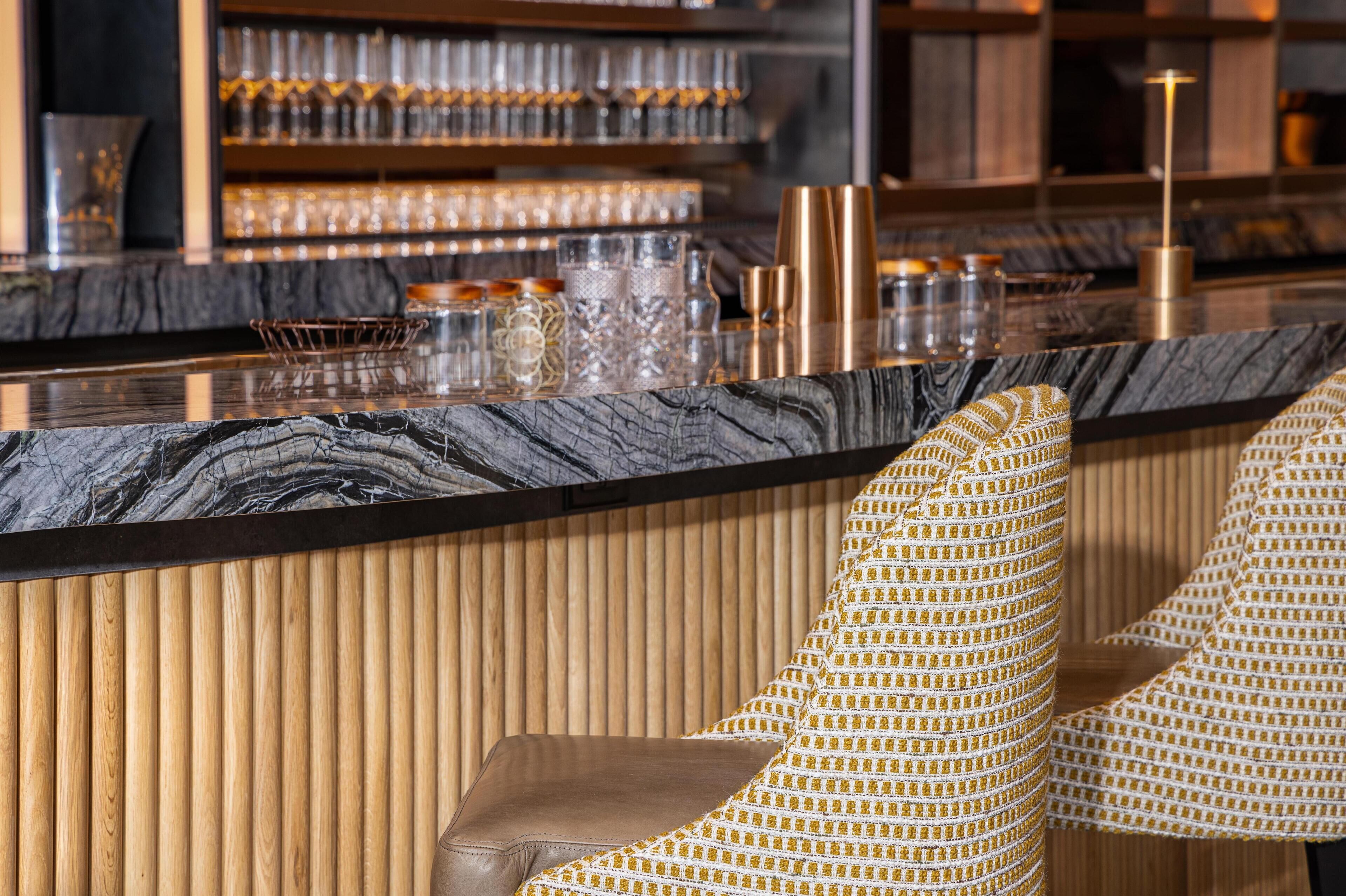 Eine Bar mit Marmorplatte, gepolsterten Sitzgelegenheiten und einer Holzvertäfelung.