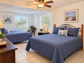A bedroom with two beds, a ceiling fan, and a painting on the wall.
