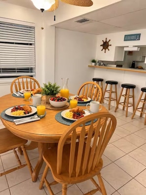 A breakfast setting with a round wooden table, chairs, and a bar area in the background. - Butler Beach Oasis - Steps To Beach - Pets Welcome (St. Augustine)