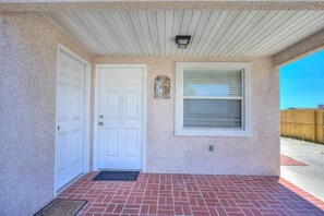 A covered porch with a brick floor, a white door, and a window with blinds. - Butler Beach Oasis - Steps To Beach - Pets Welcome (St. Augustine)