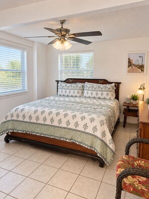 A bedroom with a bed, a ceiling fan, a nightstand with a lamp, and a window with blinds. - Butler Beach Oasis - Steps To Beach - Pets Welcome (St. Augustine)