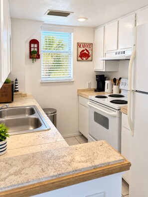 A compact kitchen with white cabinets, a double sink, a stove, and a refrigerator.